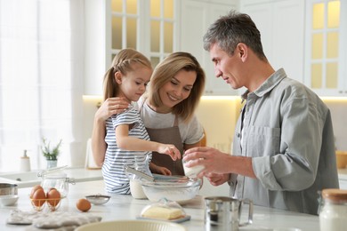 Photo of Happy parents and their daughter making dough at white marble table in kitchen