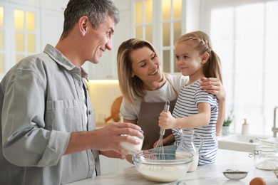 Photo of Happy parents and their daughter making dough at white marble table in kitchen