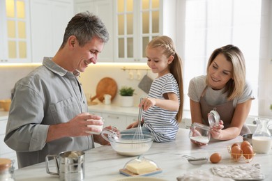 Photo of Happy parents and their daughter making dough at white marble table in kitchen