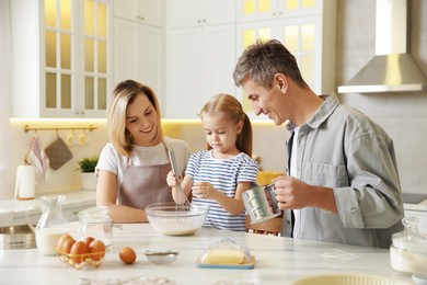 Photo of Happy parents and their daughter making dough at white marble table in kitchen