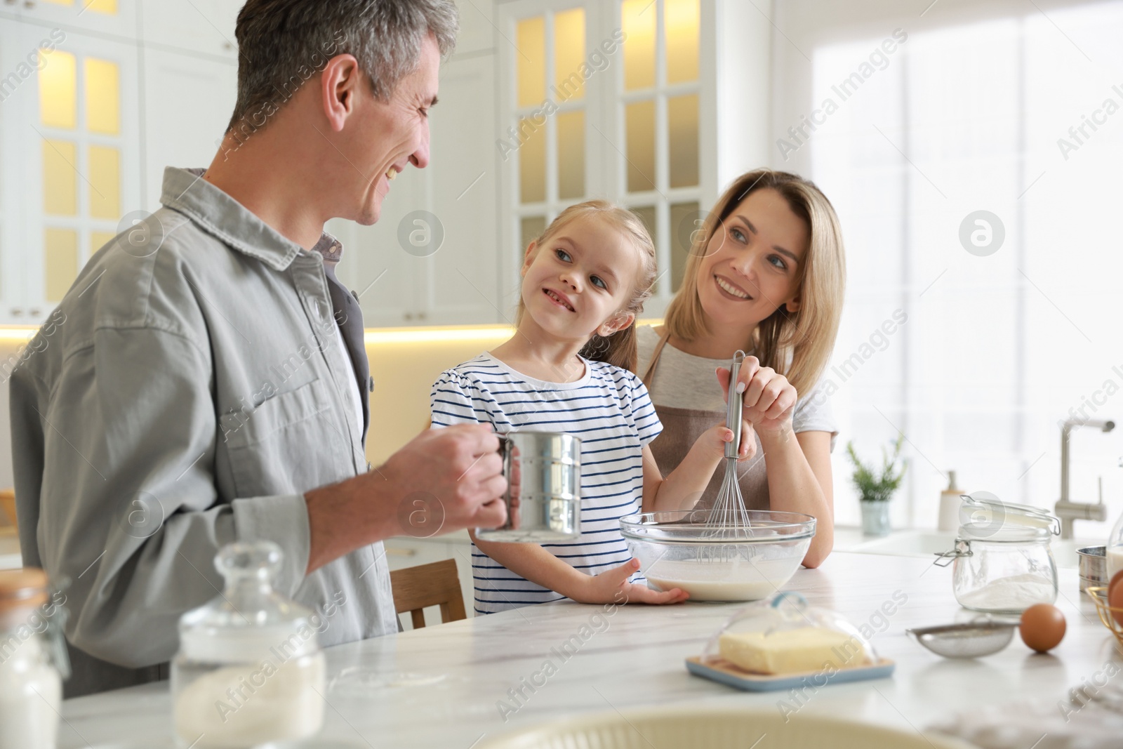 Photo of Happy parents and their daughter making dough at white marble table in kitchen