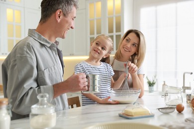 Happy parents and their daughter making dough at white marble table in kitchen