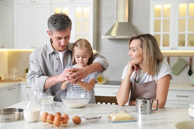 Photo of Happy parents and their daughter making dough at white marble table in kitchen