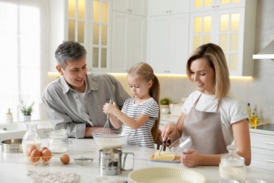 Photo of Happy parents and their daughter making dough at white marble table in kitchen