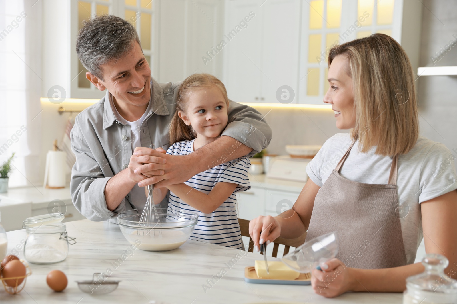 Photo of Happy parents and their daughter making dough at white marble table in kitchen