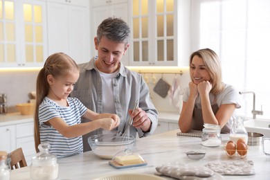 Photo of Happy parents and their daughter making dough at white marble table in kitchen