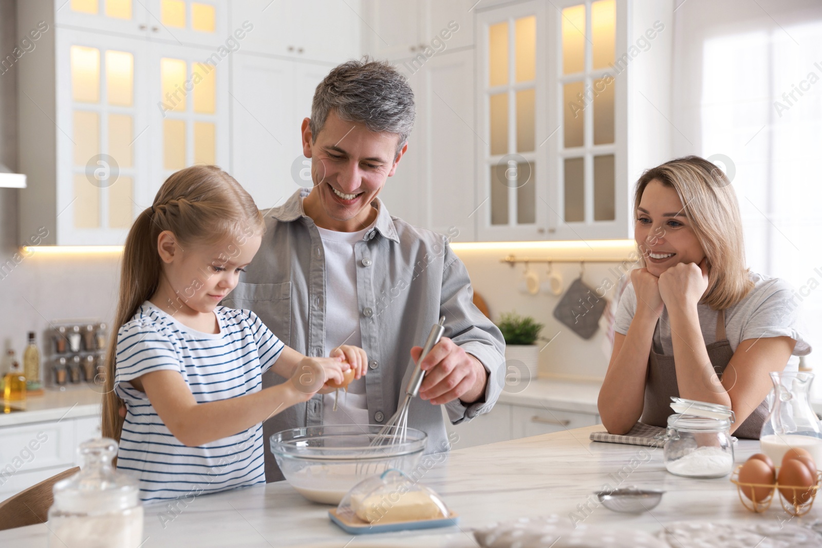 Photo of Happy parents and their daughter making dough at white marble table in kitchen