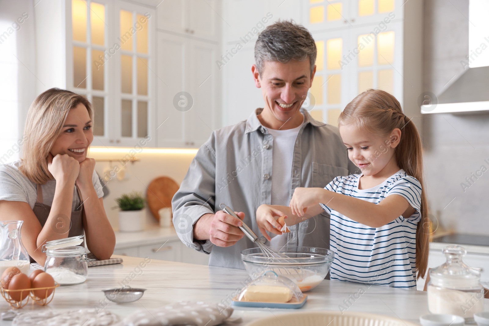 Photo of Happy parents and their daughter making dough at white marble table in kitchen