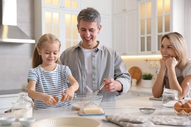 Photo of Happy parents and their daughter making dough at white marble table in kitchen