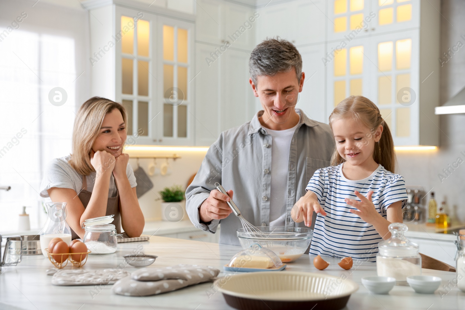 Photo of Happy parents and their daughter making dough at white marble table in kitchen