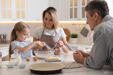 Photo of Happy parents and their daughter making dough at white marble table in kitchen