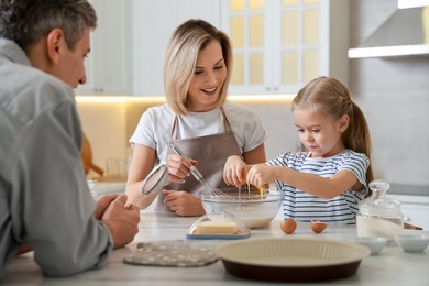 Photo of Happy parents and their daughter making dough at white marble table in kitchen