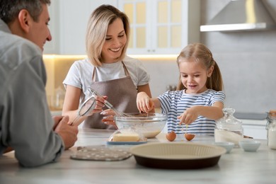 Photo of Happy parents and their daughter making dough at white marble table in kitchen