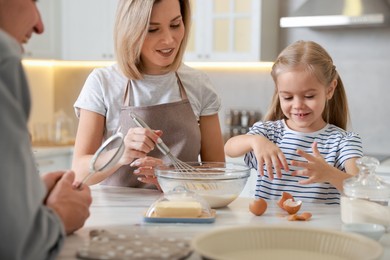 Photo of Happy parents and their daughter making dough at white marble table in kitchen