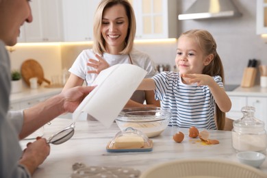 Photo of Happy parents and their daughter making dough at white marble table in kitchen