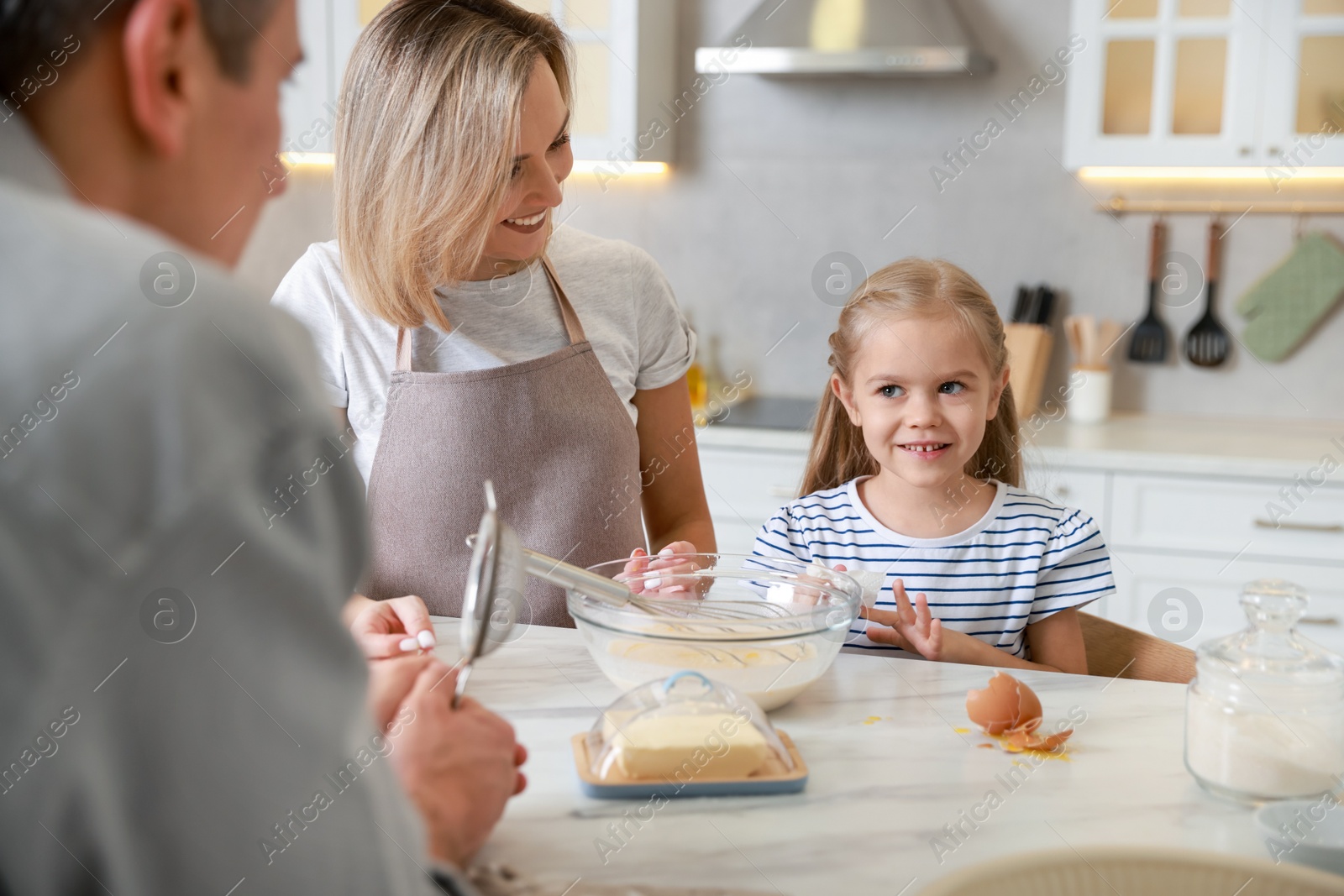 Photo of Happy parents and their daughter making dough at white marble table in kitchen