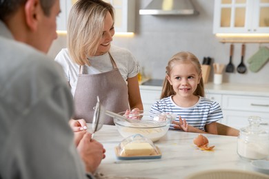 Photo of Happy parents and their daughter making dough at white marble table in kitchen