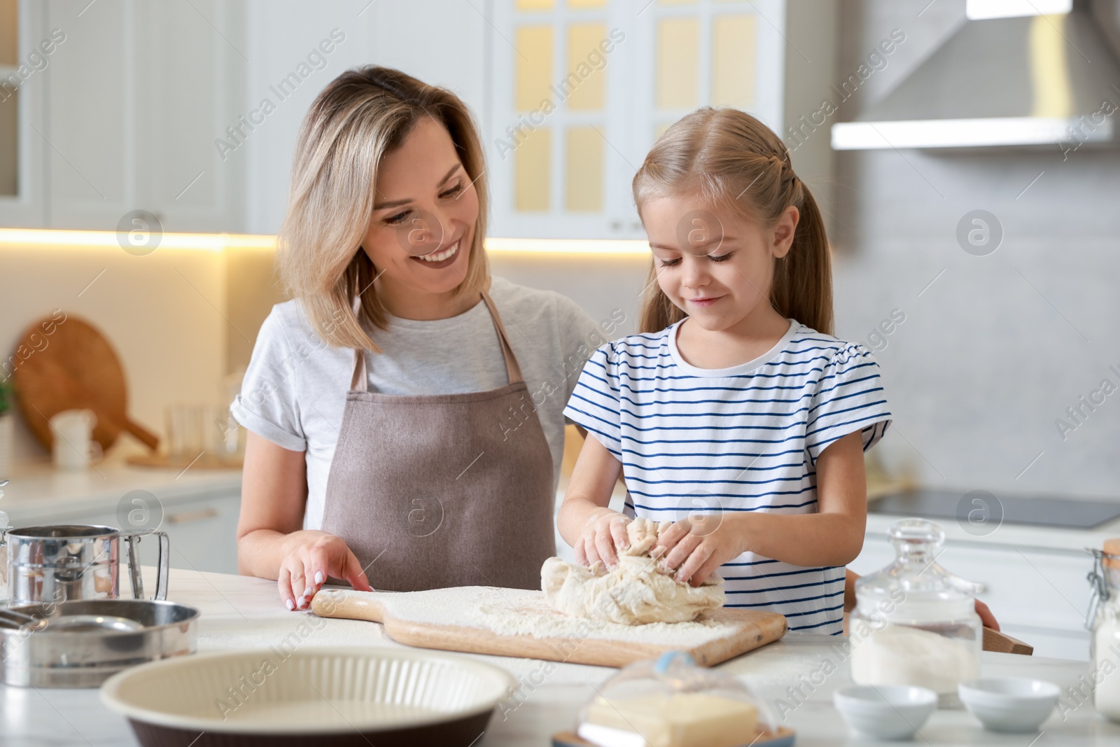 Photo of Mother and her daughter kneading dough at table in kitchen