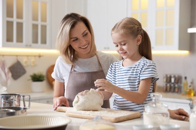 Mother and her daughter kneading dough at table in kitchen