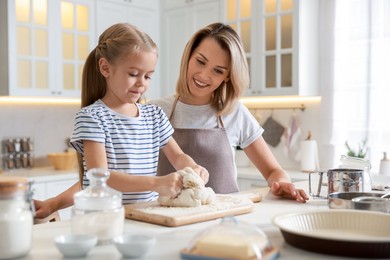 Photo of Mother and her daughter kneading dough at table in kitchen