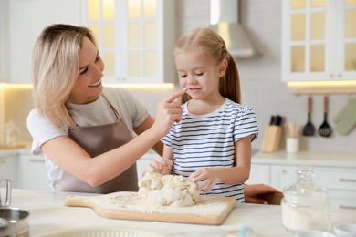 Photo of Mother and her daughter kneading dough at table in kitchen