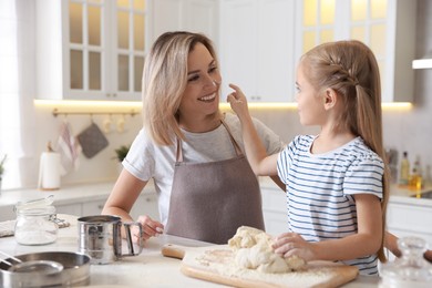 Photo of Mother and her daughter kneading dough at table in kitchen