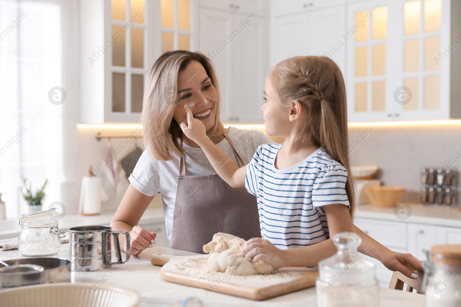 Photo of Mother and her daughter kneading dough at table in kitchen