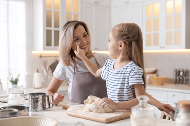 Photo of Mother and her daughter kneading dough at table in kitchen