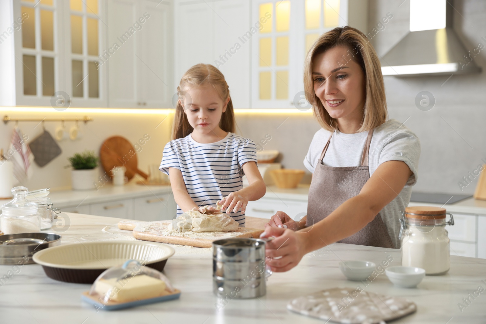 Photo of Mother and her daughter making dough at white marble table in kitchen