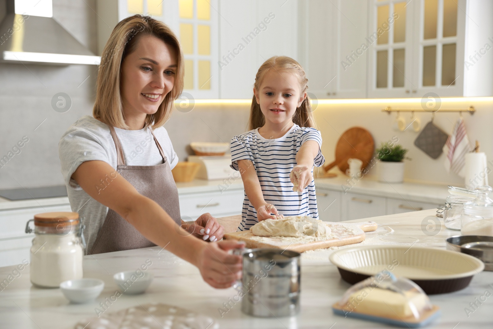 Photo of Mother and her daughter making dough at white marble table in kitchen