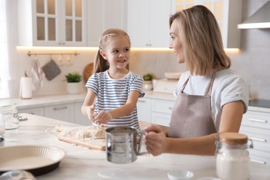 Photo of Mother and her daughter making dough at white marble table in kitchen