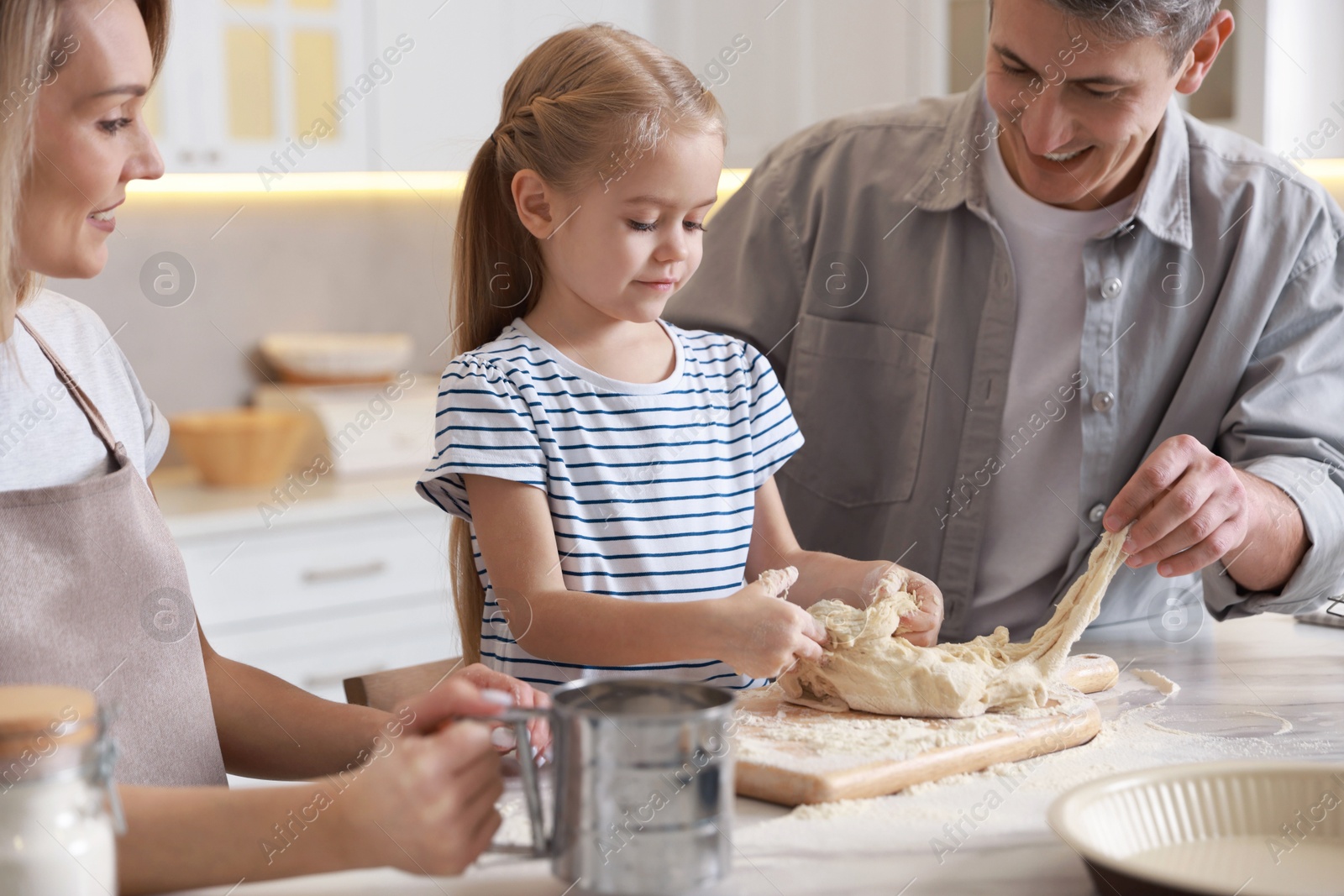 Photo of Happy parents and their daughter making dough at white marble table in kitchen