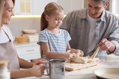 Photo of Happy parents and their daughter making dough at white marble table in kitchen