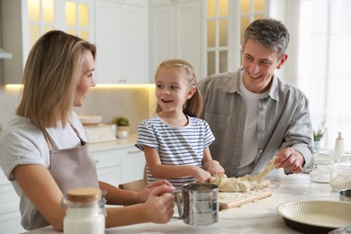 Photo of Happy parents and their daughter making dough at white marble table in kitchen