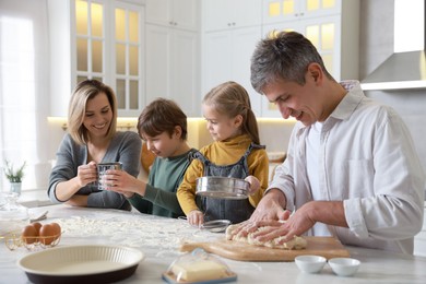 Photo of Happy family making dough at white marble table in kitchen