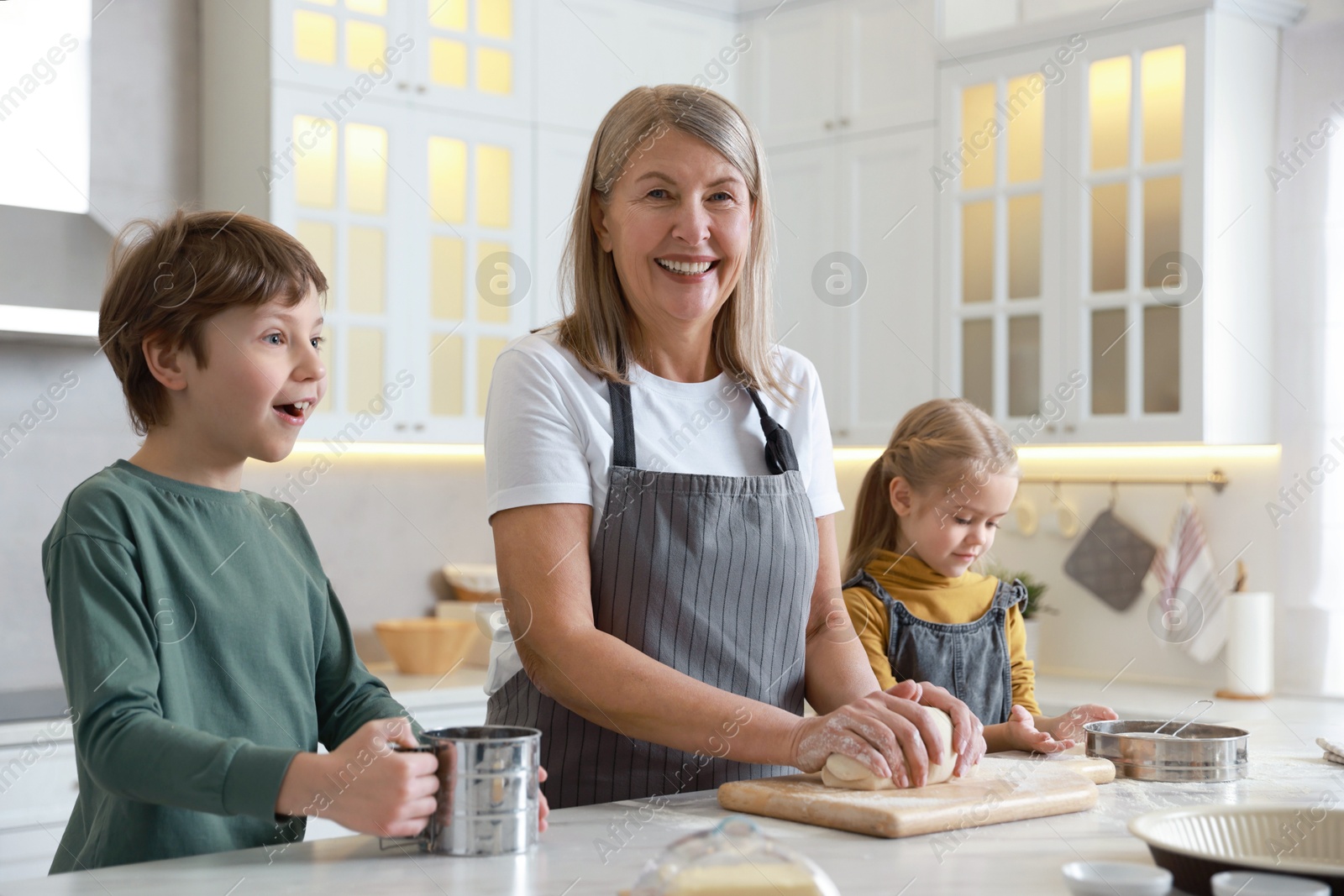 Photo of Grandmother and her grandchildren making dough at white marble table in kitchen