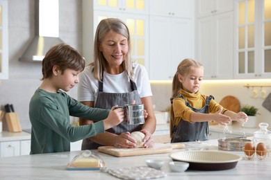 Photo of Grandmother and her grandchildren making dough at white marble table in kitchen