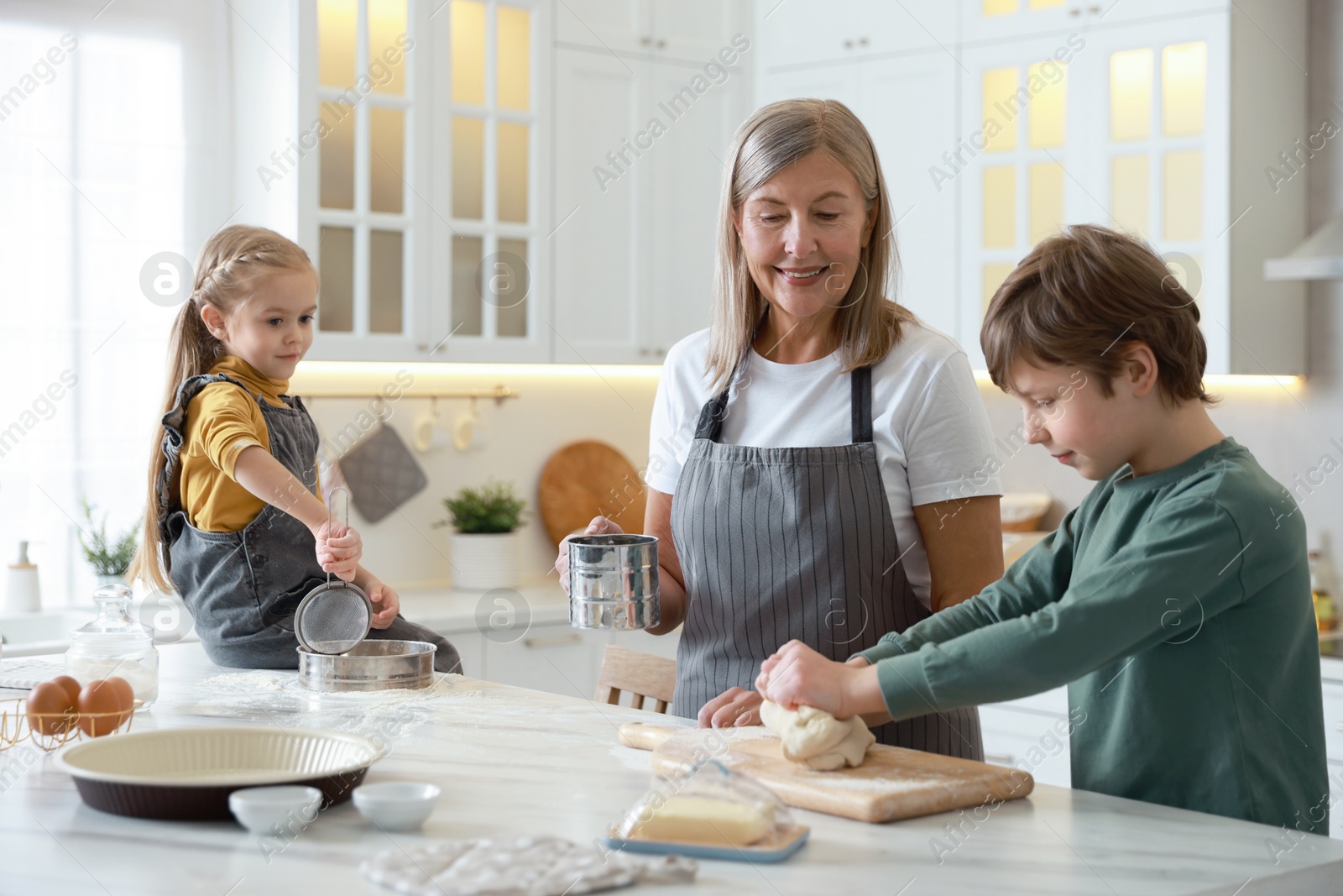 Photo of Grandmother and her grandchildren making dough at white marble table in kitchen