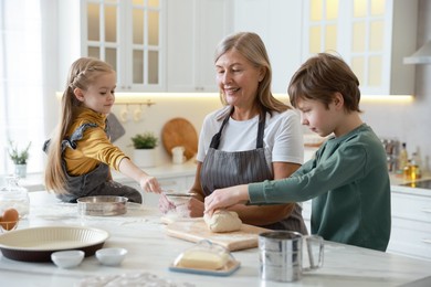 Photo of Grandmother and her grandchildren making dough at white marble table in kitchen