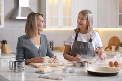 Photo of Mother and her daughter making dough at white marble table in kitchen