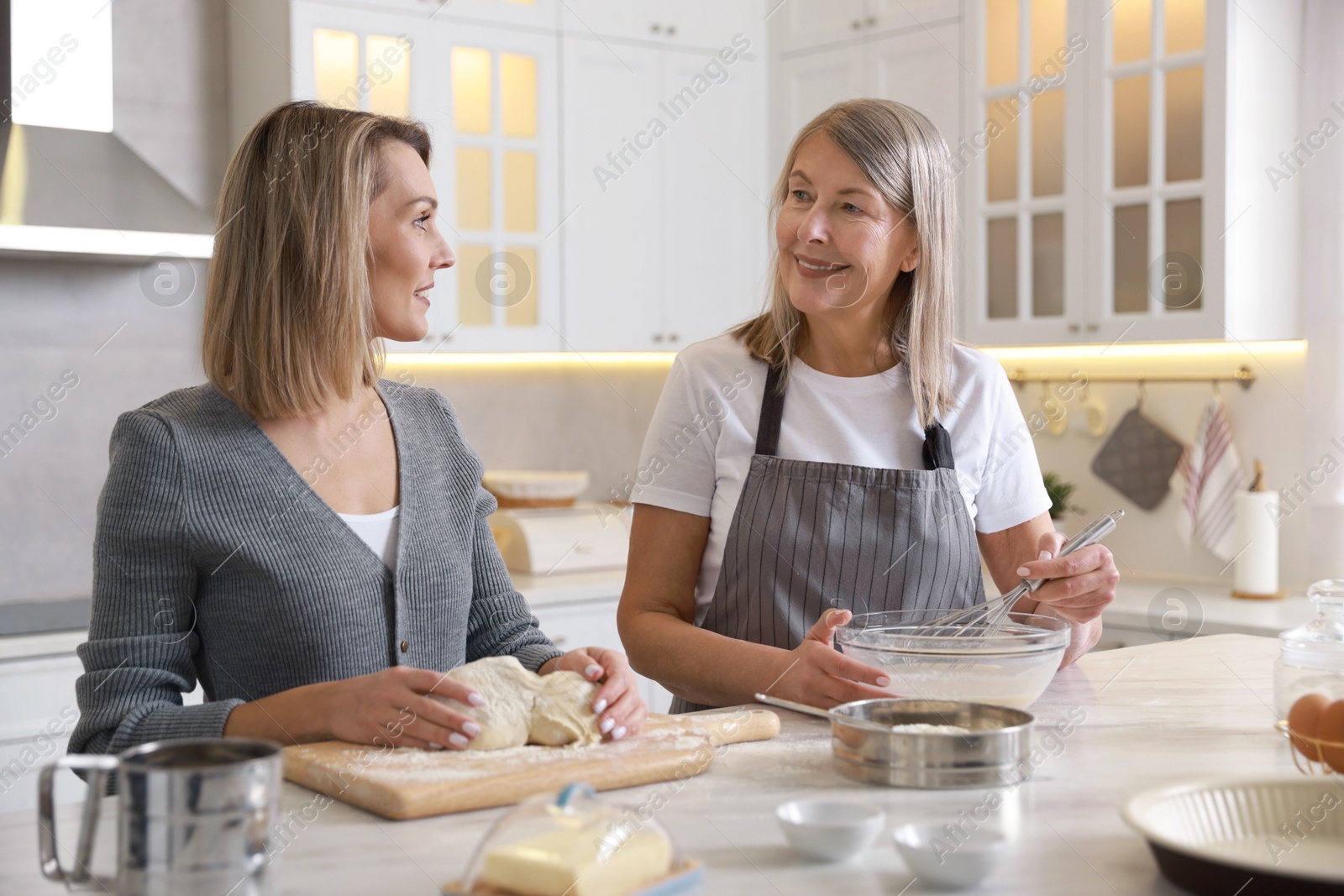 Photo of Mother and her daughter making dough at white marble table in kitchen