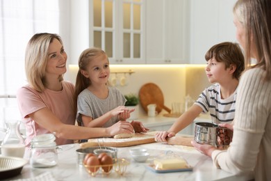 Photo of Little kids with their mother and grandmother making dough at white marble table in kitchen