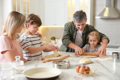 Photo of Happy family making dough at white marble table in kitchen