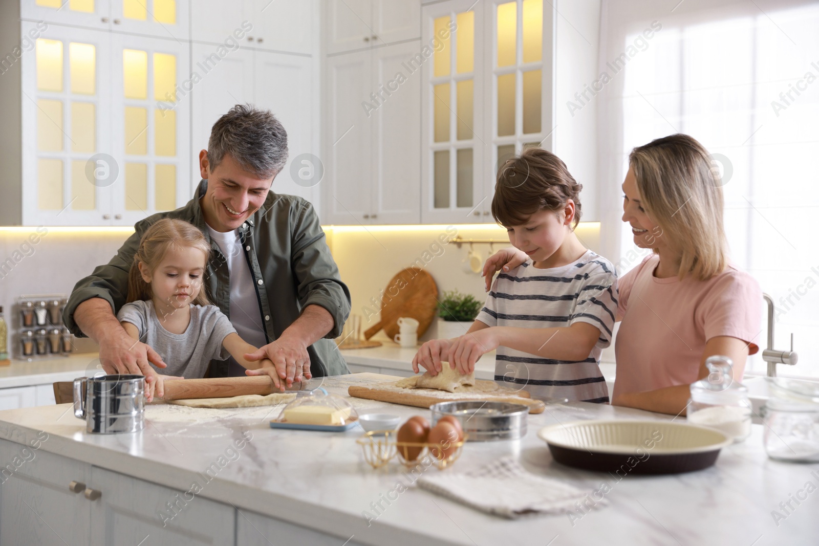 Photo of Happy family making dough at white marble table in kitchen