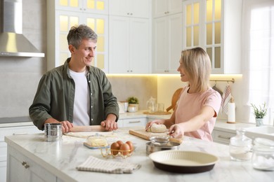 Photo of Happy couple kneading dough at white marble table in kitchen