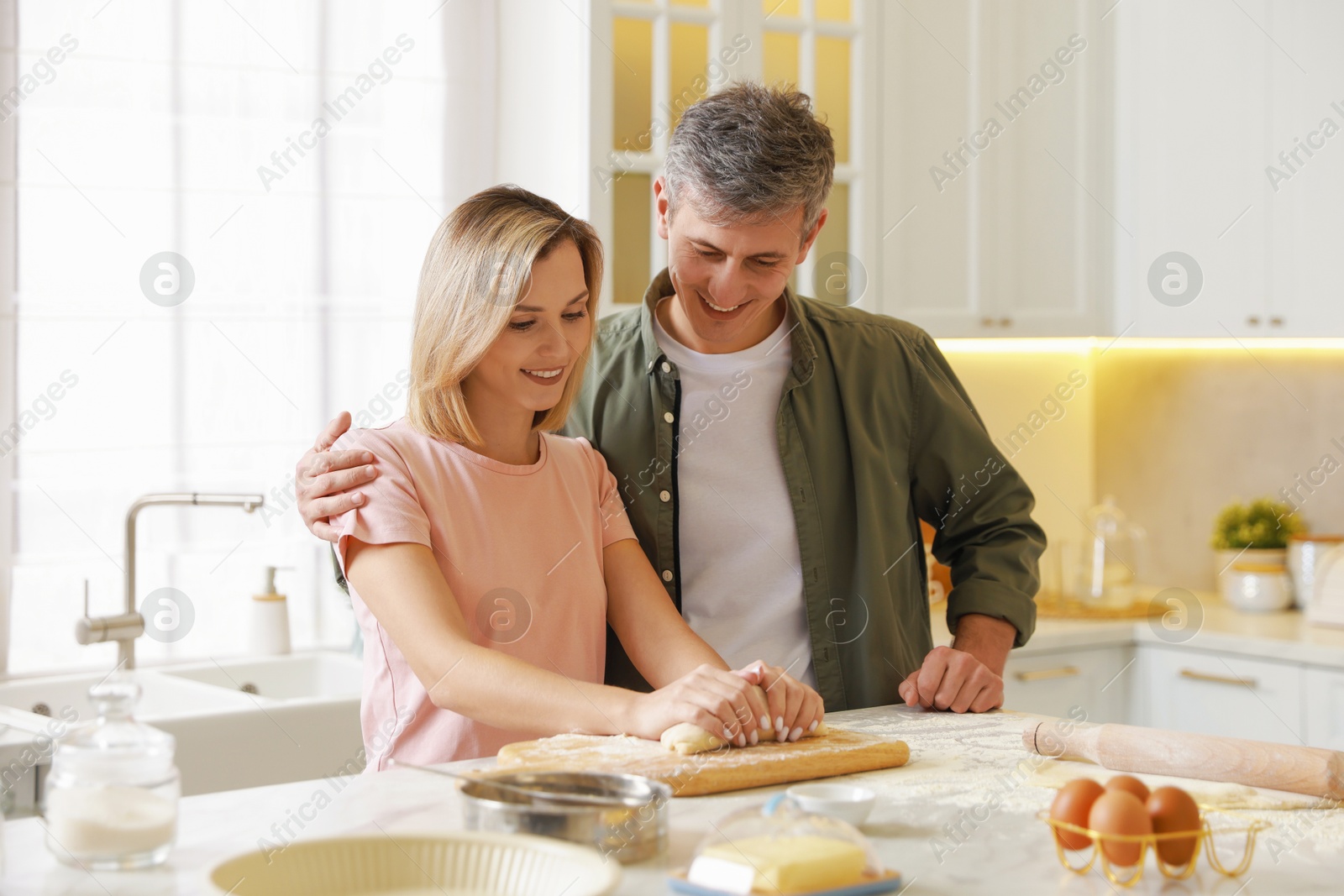 Photo of Happy couple kneading dough at white marble table in kitchen