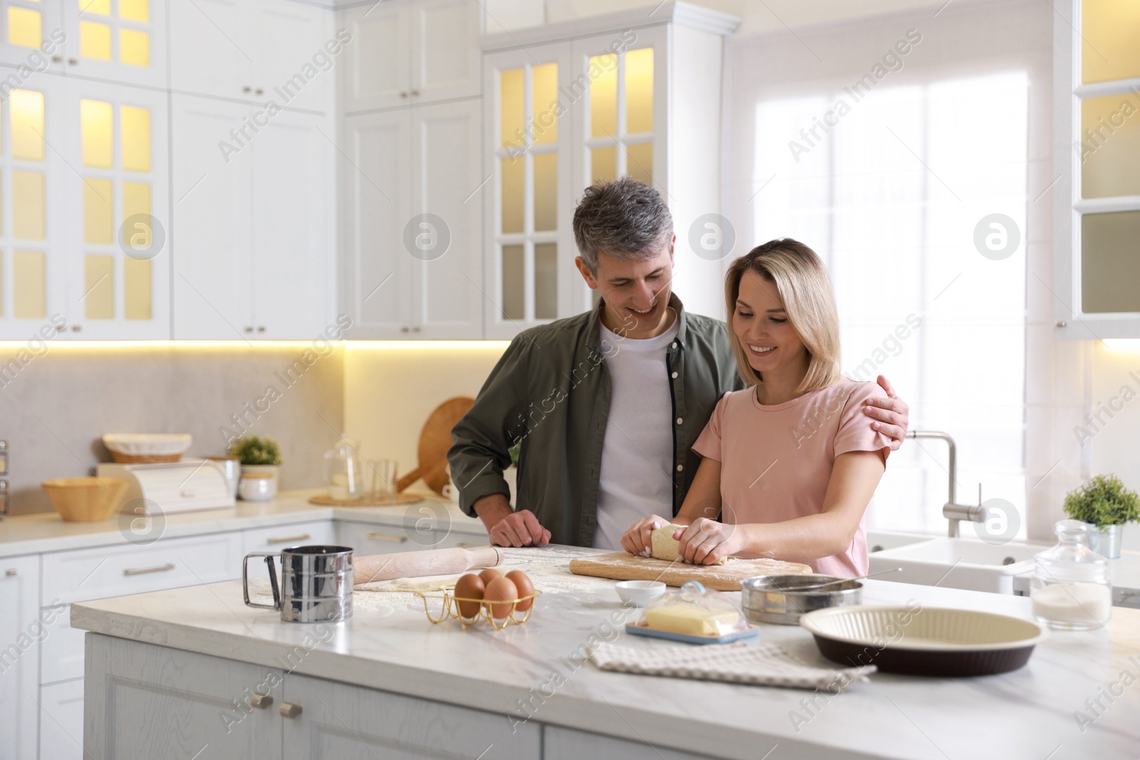 Photo of Happy couple kneading dough at white marble table in kitchen