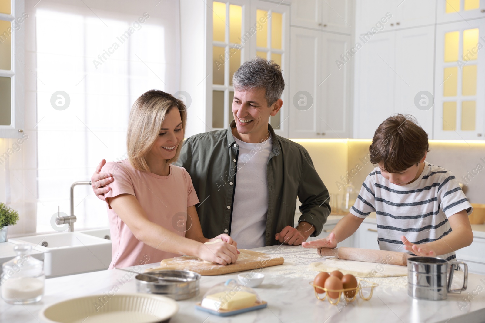 Photo of Happy family kneading dough at white marble table in kitchen