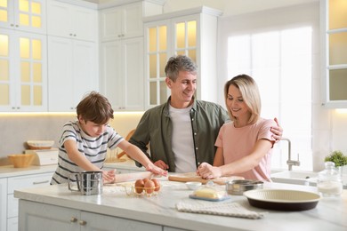 Happy family kneading dough at white marble table in kitchen