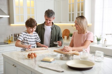 Photo of Happy family kneading dough at white marble table in kitchen